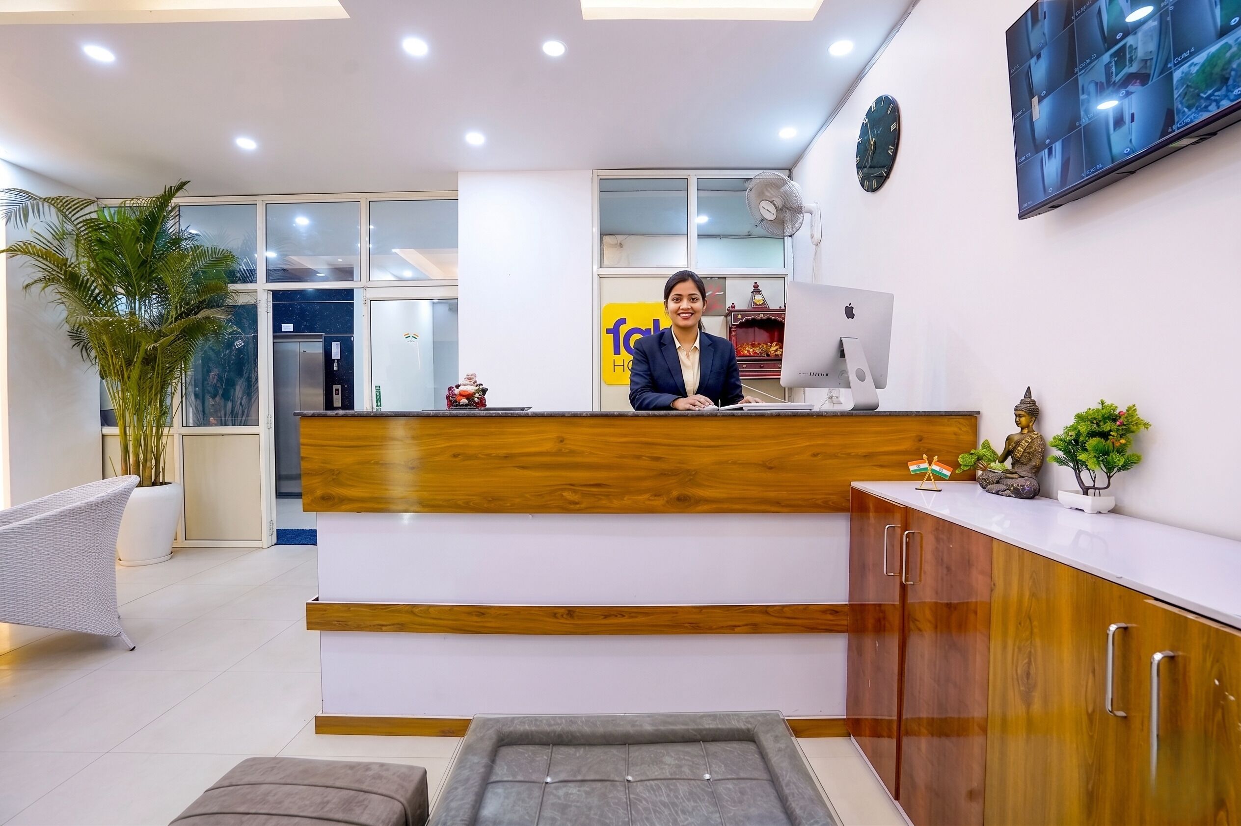 Zona de recepción con mostrador de madera, una computadora, un reloj y un televisor mostrando varias pantallas.