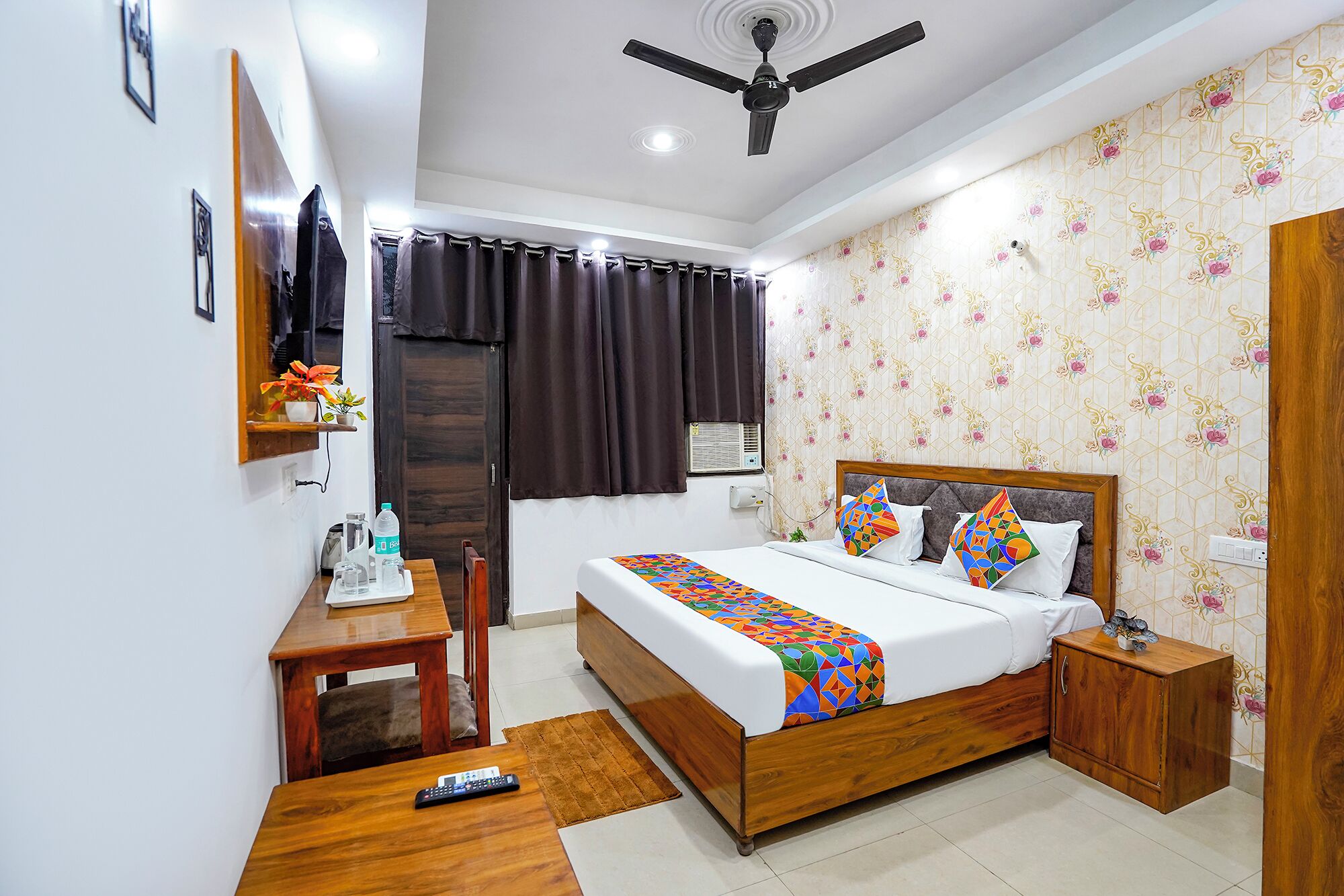 A bedroom with a wooden bed, a desk, a chair, a ceiling fan, and a window with curtains.