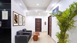 A reception area with a reception desk, a sofa, framed artwork on the walls, a wooden table, and a potted plant. - FabHotel Frolic Luxury Stay (Noida)