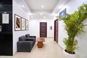 A reception area with a reception desk, a sofa, framed artwork on the walls, a wooden table, and a potted plant. - FabHotel Frolic Luxury Stay (Noida)