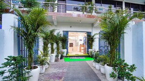 A hotel entrance with a green carpet, potted plants, and a blue railing. - FabHotel Frolic Luxury Stay (Noida)