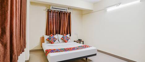 A hotel room with a bed, curtains, a ceiling fan, and a bedside table.