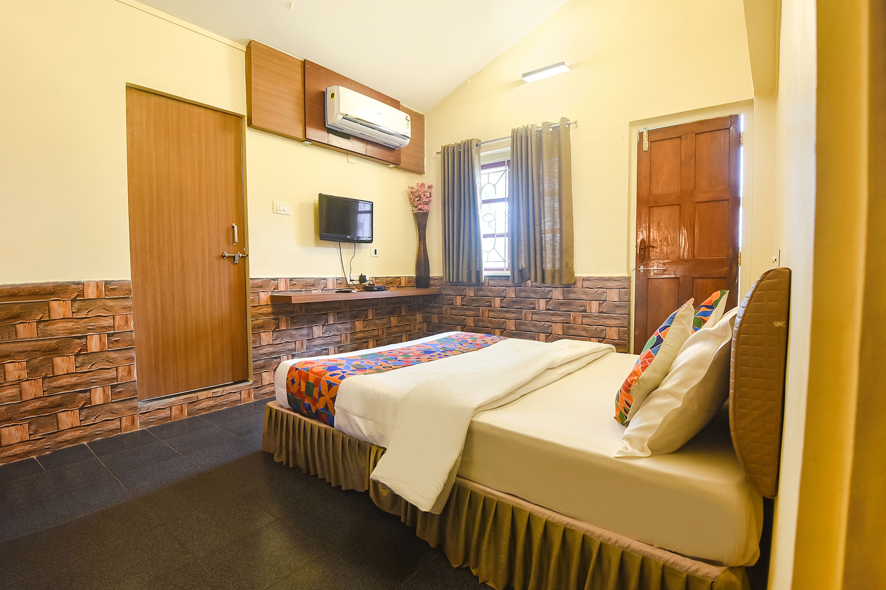 A hotel room with a bed, a TV, an air conditioner, and a window with curtains.