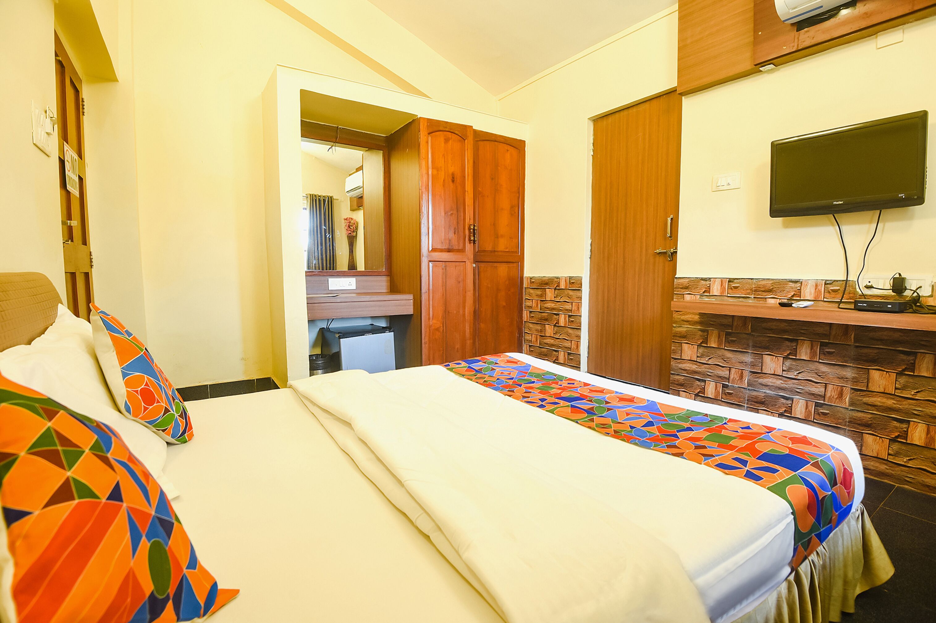 Habitación de hotel con dos camas, un armario de madera, un televisor montado en la pared y una pared con diseño de piedra.