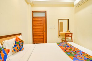 A hotel room with a bed, a wooden door, a desk with a chair, and a mirror. - Fabhotel Prime Am Suites (Hyderabad)