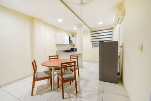 A compact kitchen with a dining table and chairs, a refrigerator, and a ceiling fan. - Fabhotel Prime Am Suites (Hyderabad)