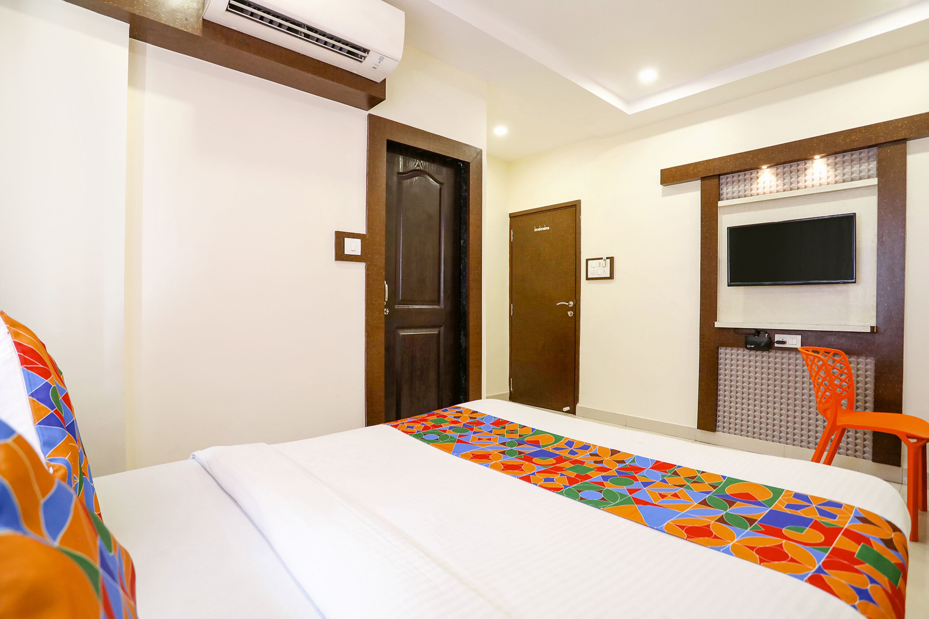 A hotel room with a bed, a TV mounted on the wall, an air conditioner, and a door.