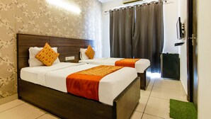 A hotel room with two beds, floral wallpaper, a ceiling fan, and a TV on the wall. - FabHotel Gazelle Inn (Gurugram)