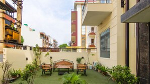 A courtyard with a green lawn, a wooden bench, and potted plants. - FabHotel Gazelle Inn (Gurugram)