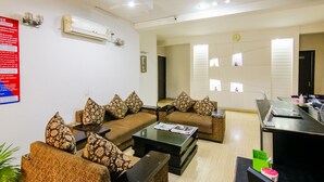 A modern living room with two sofas, a coffee table, and a dining area with a laptop and a fan. - FabHotel Gazelle Inn (Gurugram)