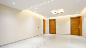 A spacious room with three wooden doors, a ceiling fan, recessed lighting, and a marble floor. - Fabhotel Raahi Retreat (Gurugram)