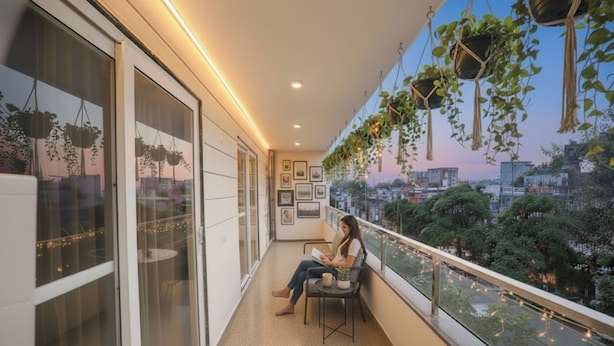 A balcony with a person sitting on a chair, a table with a cup, and hanging plants. - Fabhotel Raahi Retreat (Gurugram)