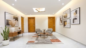 A modern lobby with a marble floor, two wooden doors, a ceiling fan, and framed artwork on the walls. - Fabhotel Raahi Retreat (Gurugram)