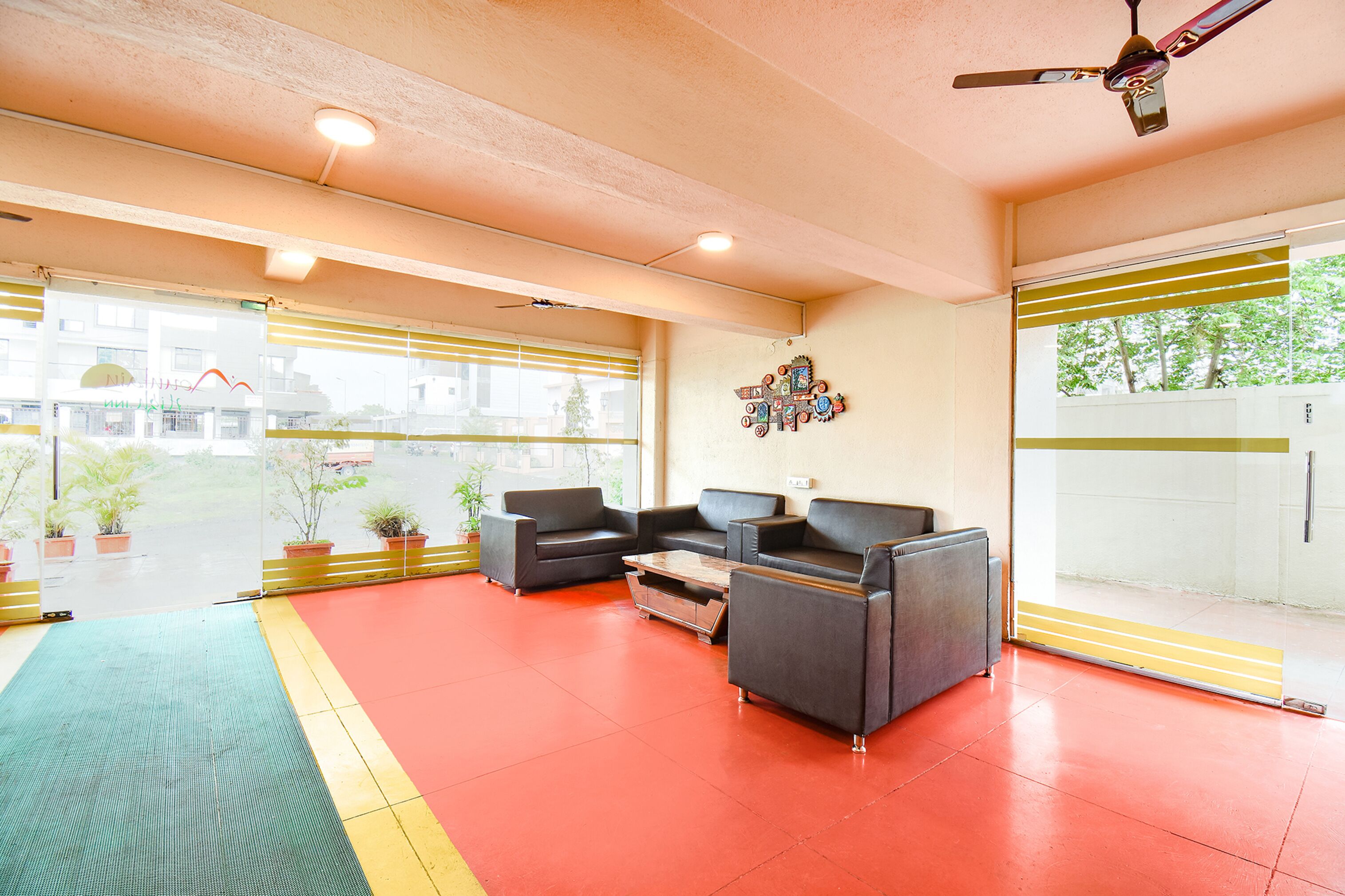 A lobby with a red floor, two grey sofas, a wooden coffee table, and a ceiling fan.
