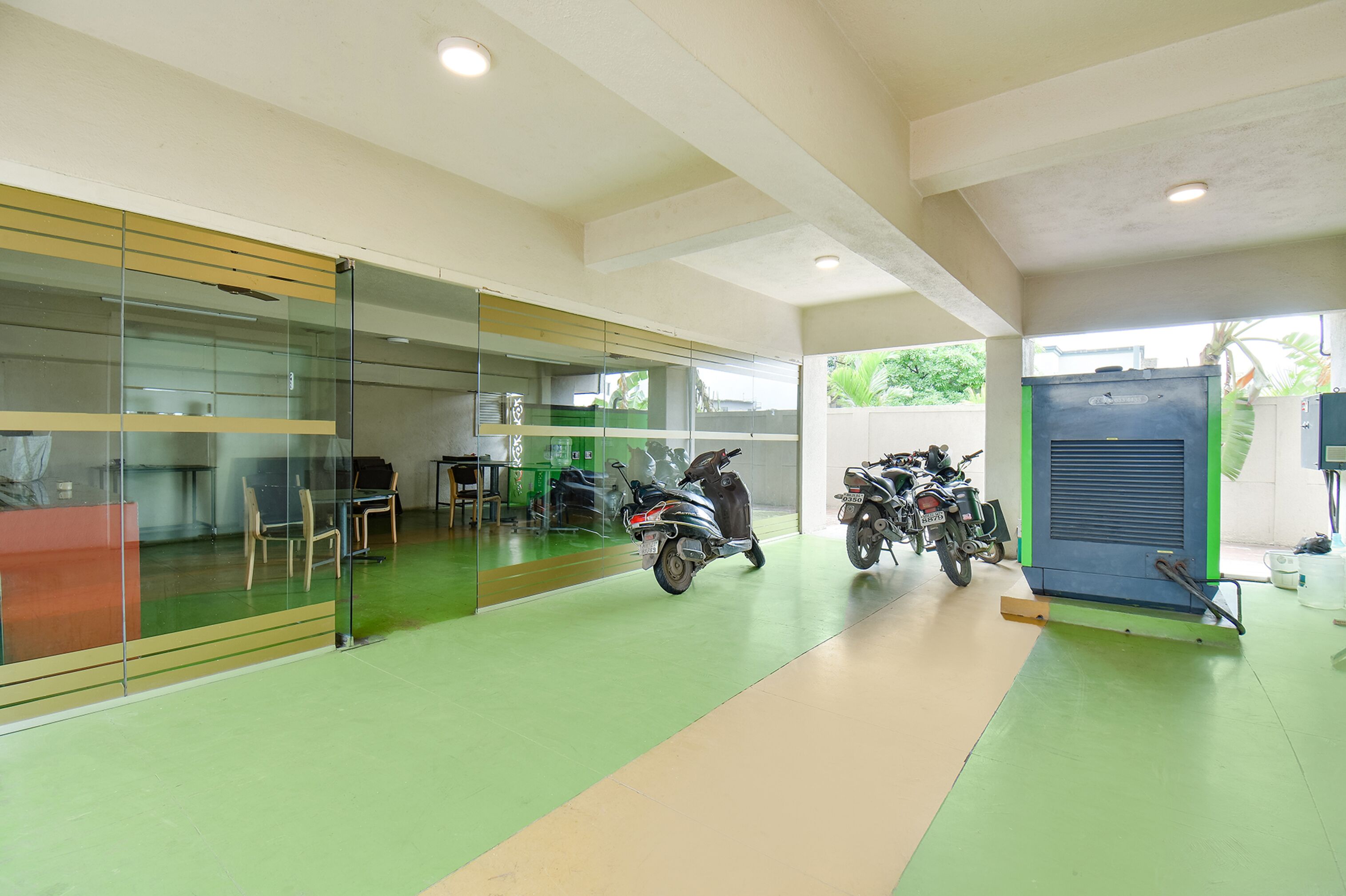 A spacious indoor area with a green floor, a glass partition, and several motorcycles parked.