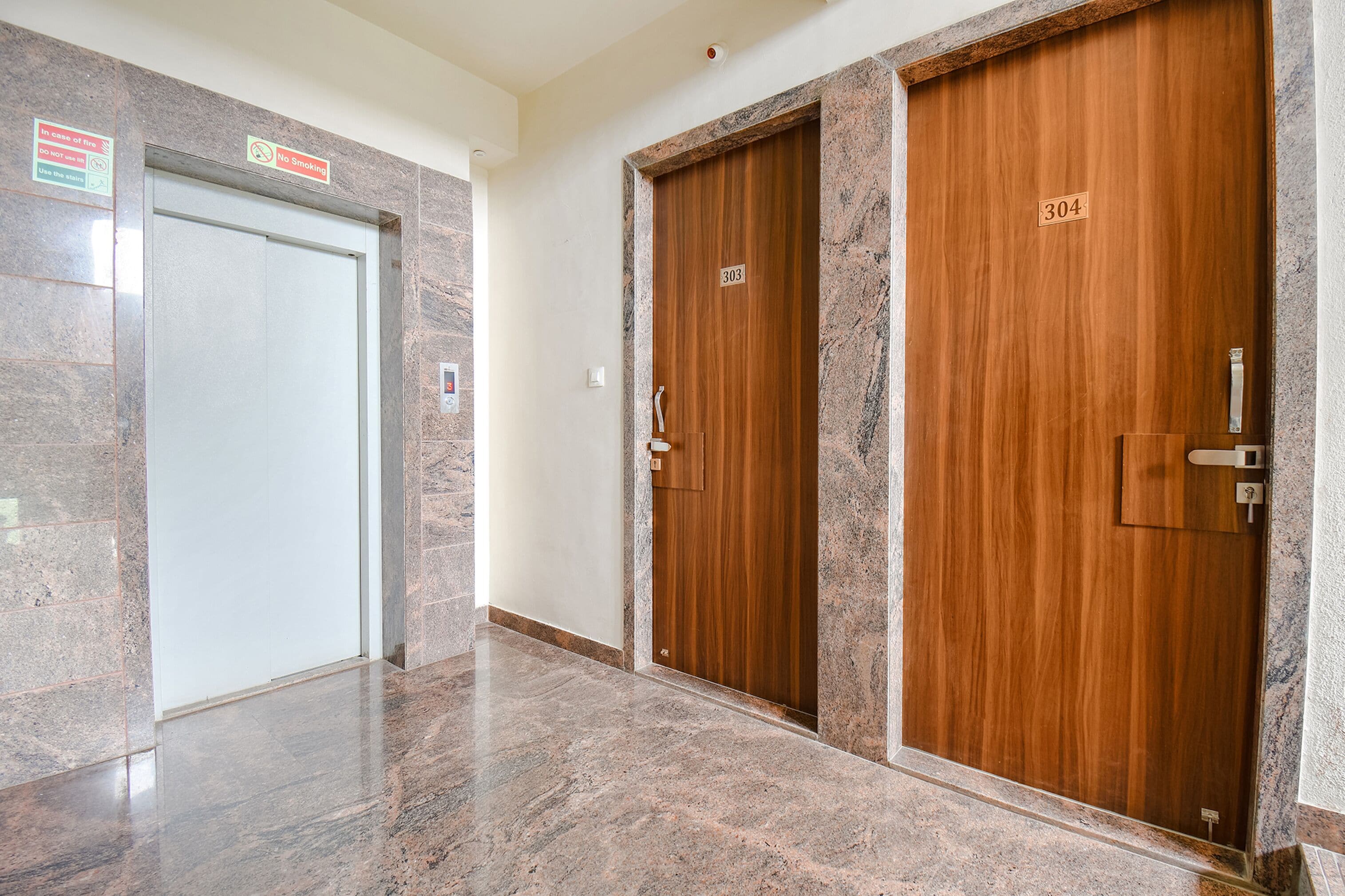 Un pasillo con piso de mármol, dos puertas de madera con la etiqueta 303 y 304, y un letrero de seguridad contra incendios en la pared izquierda.