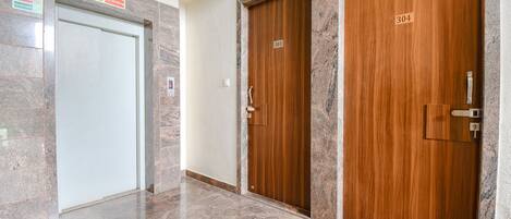 Un pasillo con piso de mármol, dos puertas de madera con la etiqueta 303 y 304, y un letrero de seguridad contra incendios en la pared izquierda.