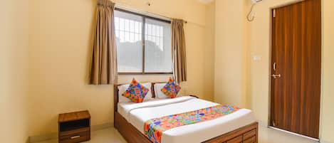 Un dormitorio con cama, una mesita de noche pequeña, una ventana con cortinas, un equipo de aire acondicionado y una puerta de madera.