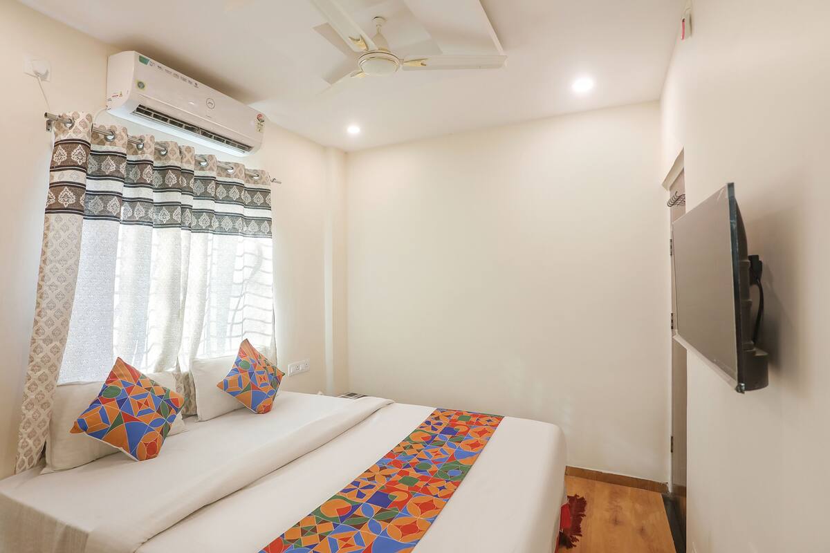 A hotel room with a bed, air conditioning unit, ceiling fan, and a television mounted on the wall.