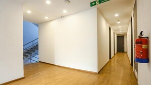A hallway with wooden flooring, white walls, and a fire extinguisher mounted on the wall. - FabExpress Meera Residency (New Delhi)