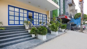 A building with blue-framed windows, a set of stairs leading to the entrance, and potted plants at the base. - FabExpress Meera Residency (New Delhi)