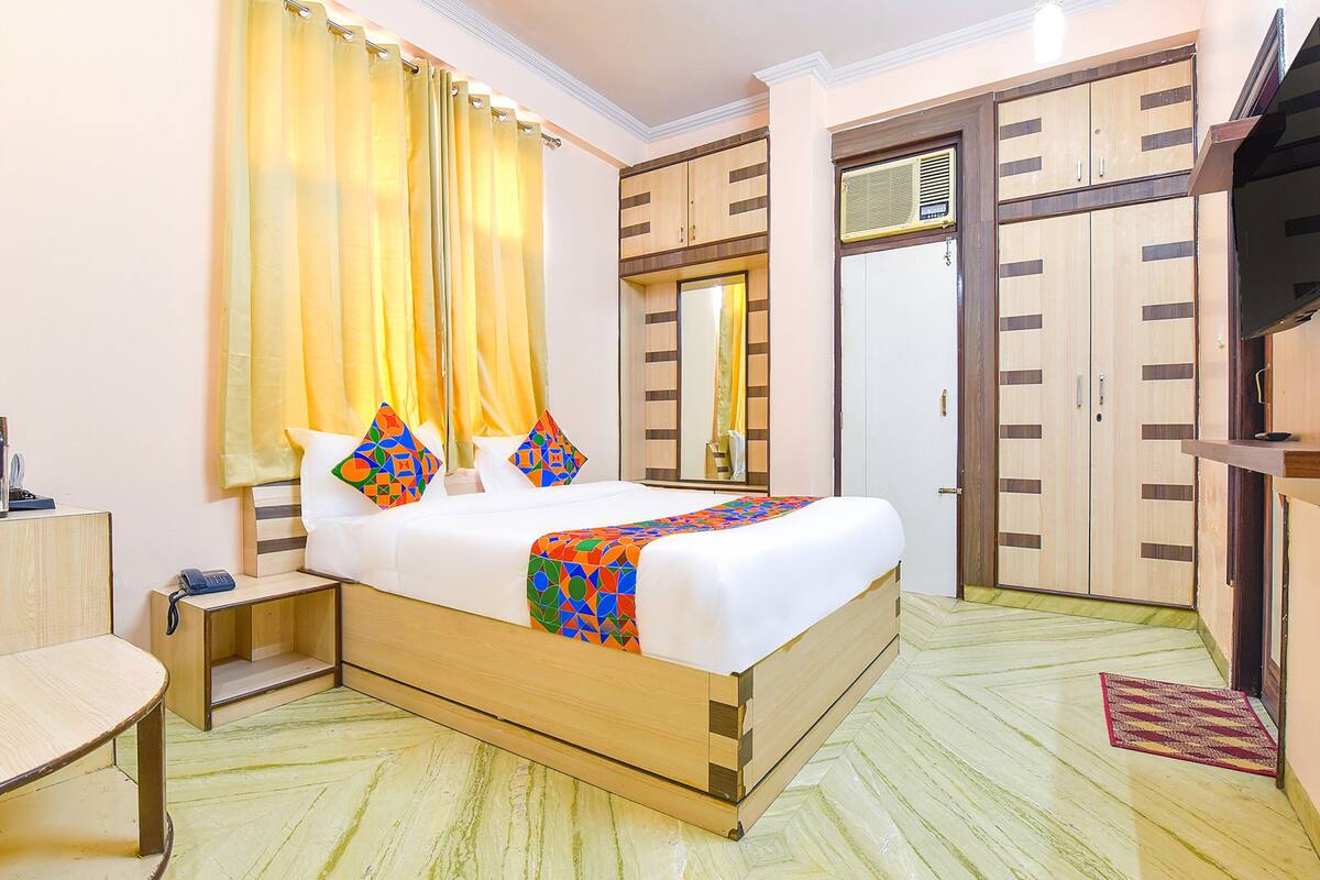 Quarto de hotel bem arrumado, com cama, mesa de cabeceira, guarda-roupa e televisão.