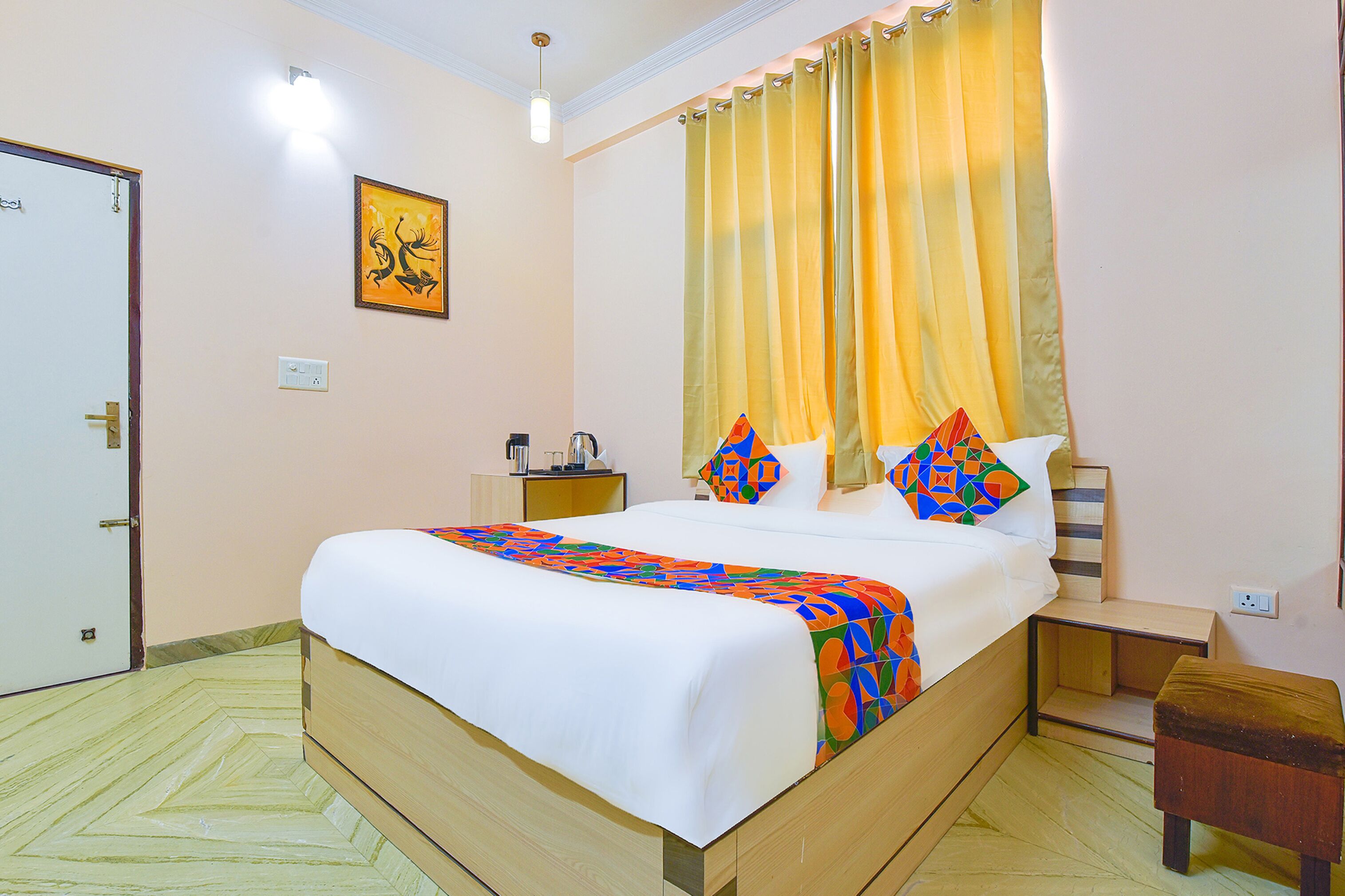 A neatly made bed with a colorful blanket, a bedside table with a lamp, and a window with yellow curtains.