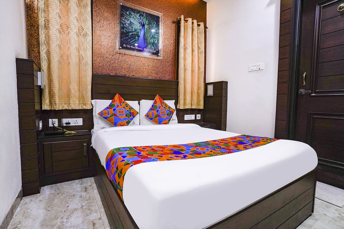 A neatly made bed with a colorful geometric-patterned bedspread, two pillows with similar patterns, a headboard with a framed picture, and a dark wooden door.