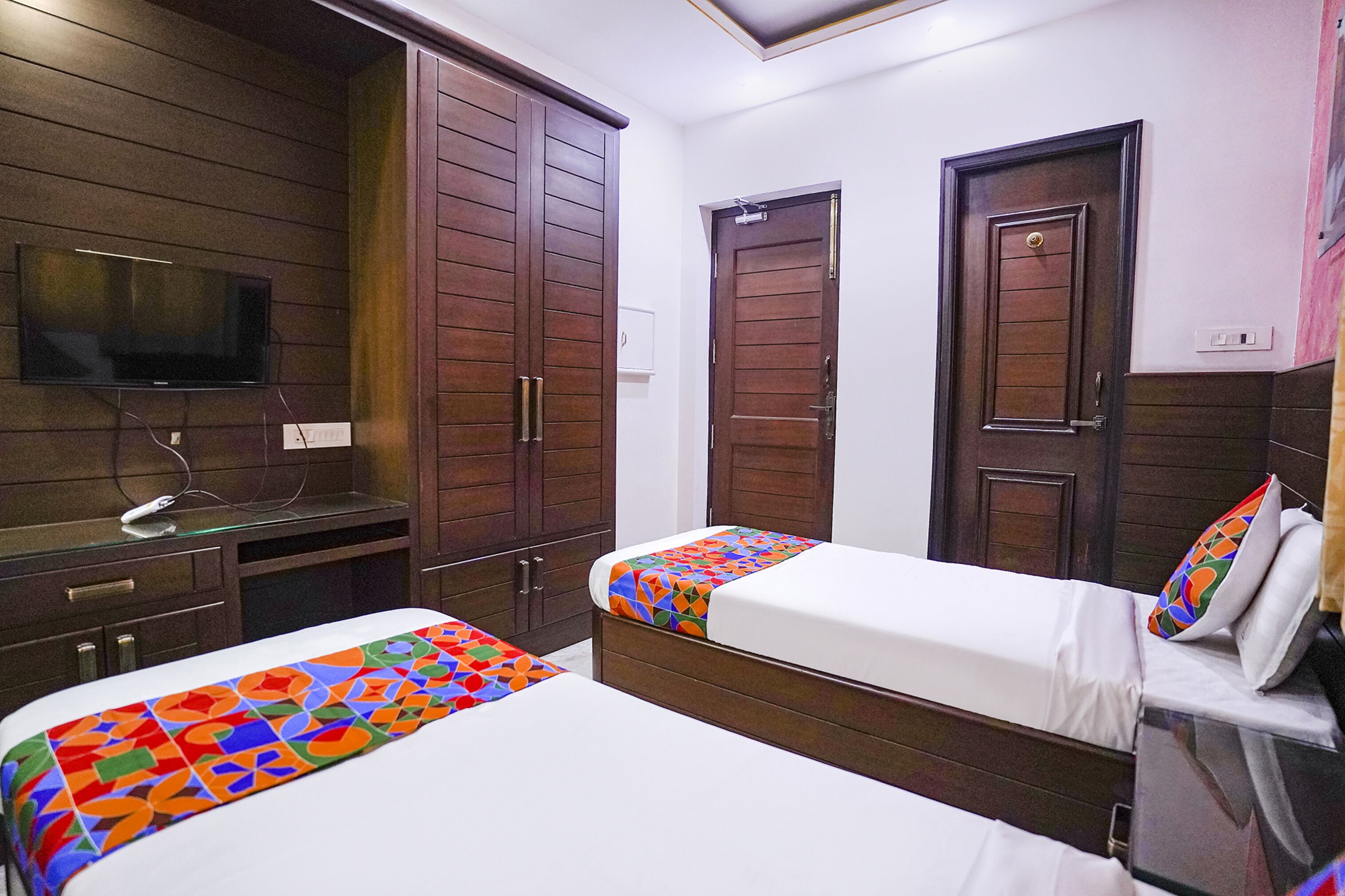 A hotel room with two beds, wooden wardrobes, a TV, and a small desk.