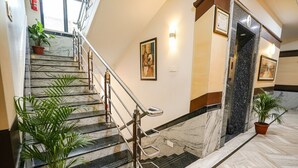 A marble staircase with metal railings and potted plants, leading to a room with a large mirror and framed artwork on the walls. - FabHotel MM Residency (Chennai)