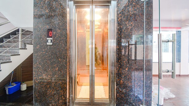 An elevator with a digital display, granite walls, and a glass door. - Fabhotel The Lily (Kolkata)