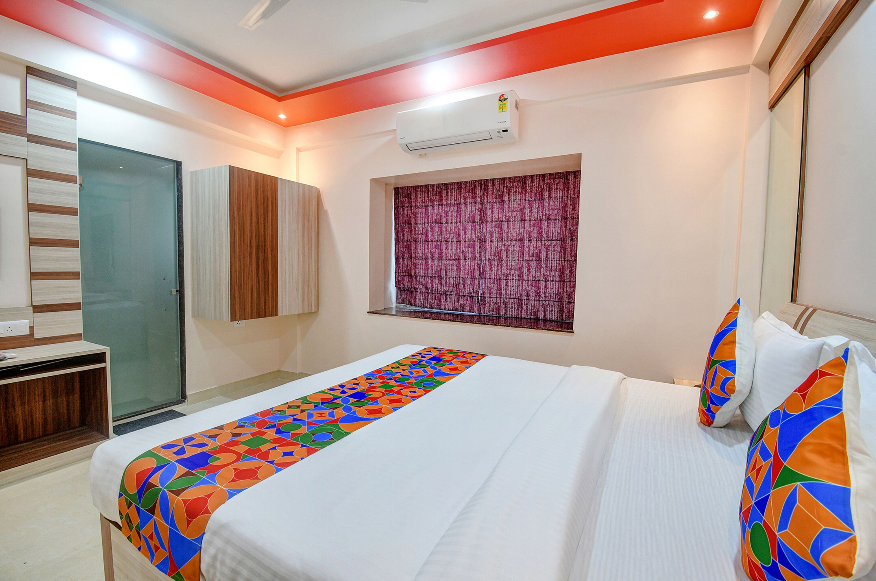 A hotel room with a bed, a wardrobe, a window with curtains, and an air conditioning unit.
