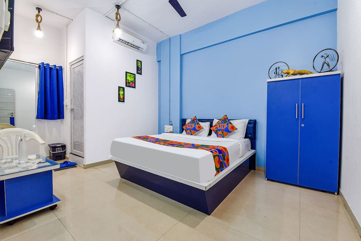 A bedroom with a bed, a blue wardrobe, a desk with a chair, and a mirror.