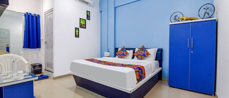 A bedroom with a bed, a blue wardrobe, a desk with a chair, and a mirror.