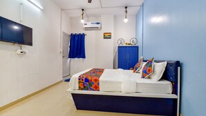 A hotel room with a bed, a TV mounted on the wall, an air conditioning unit, and a blue curtain. - Fabexpress Solitaire (Surat)