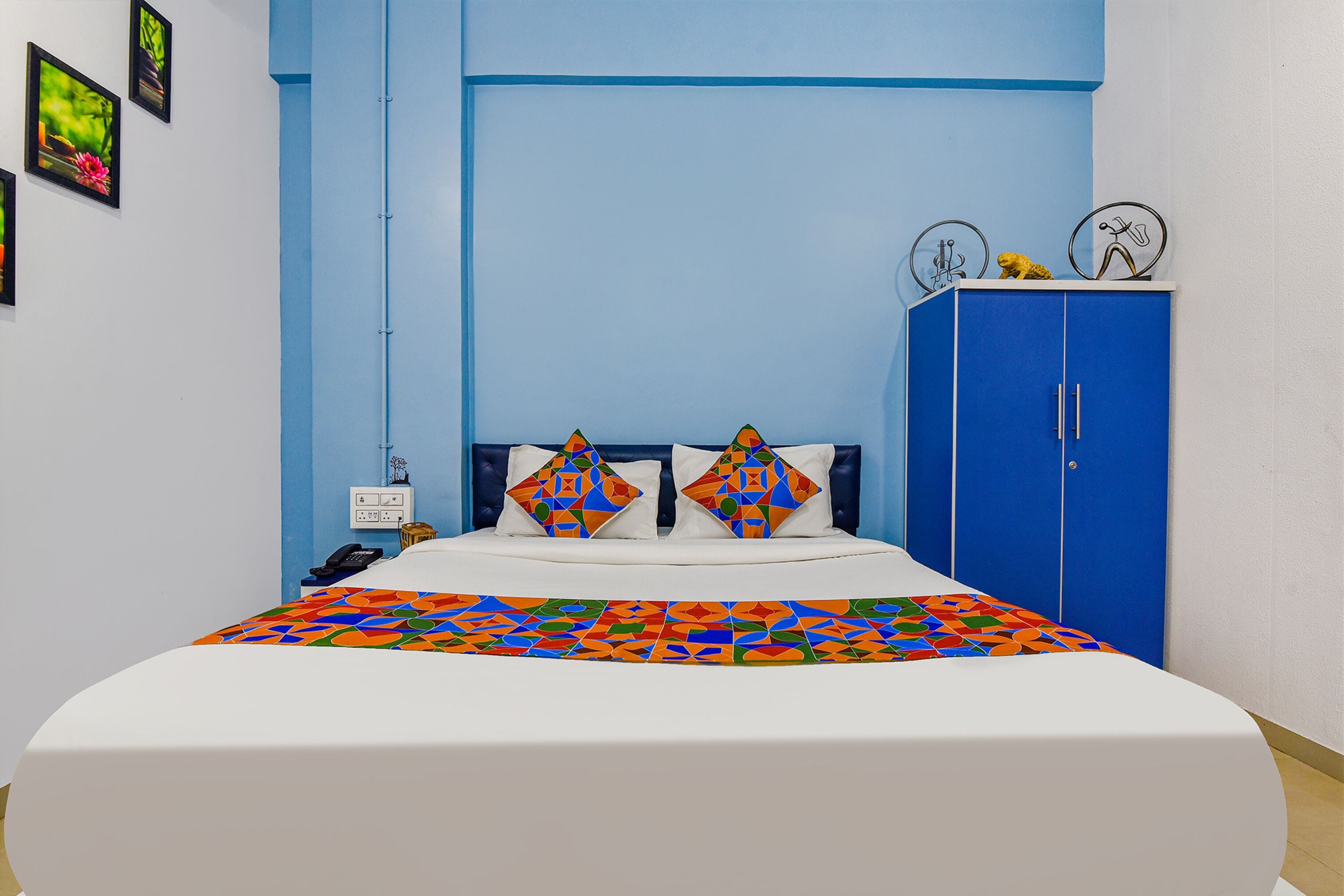 A bedroom with a bed, a blue wardrobe, and a wall with framed pictures.