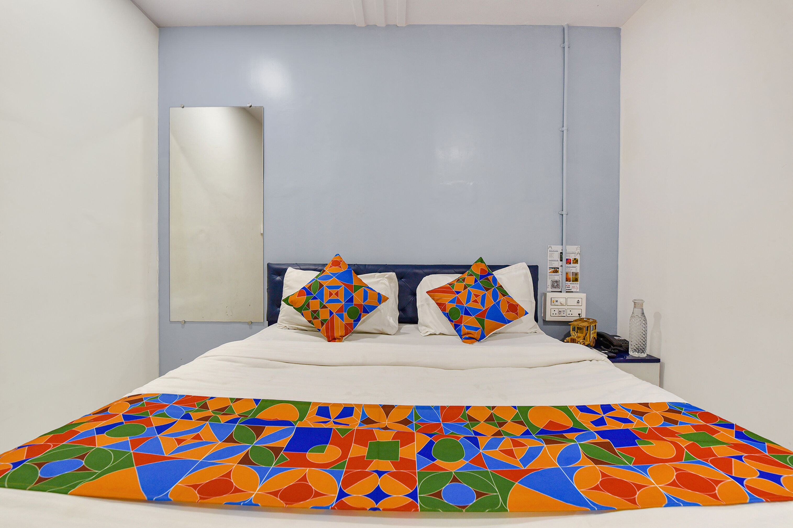 A hotel room with a bed, two pillows, a nightstand, and a wall-mounted phone.