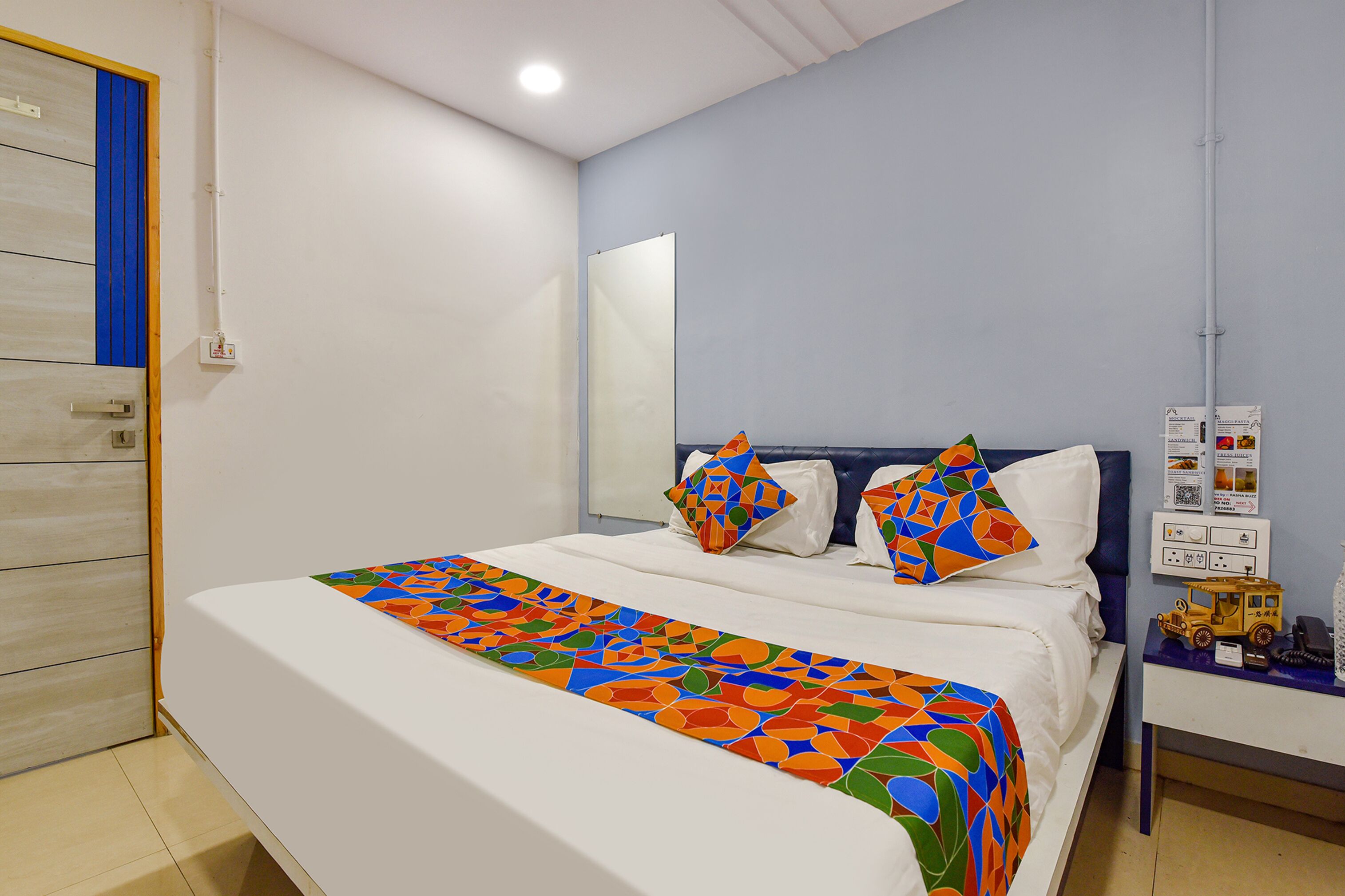 A neatly made bed with a colorful bedspread, a headboard, and a bedside table with a toy and a phone.