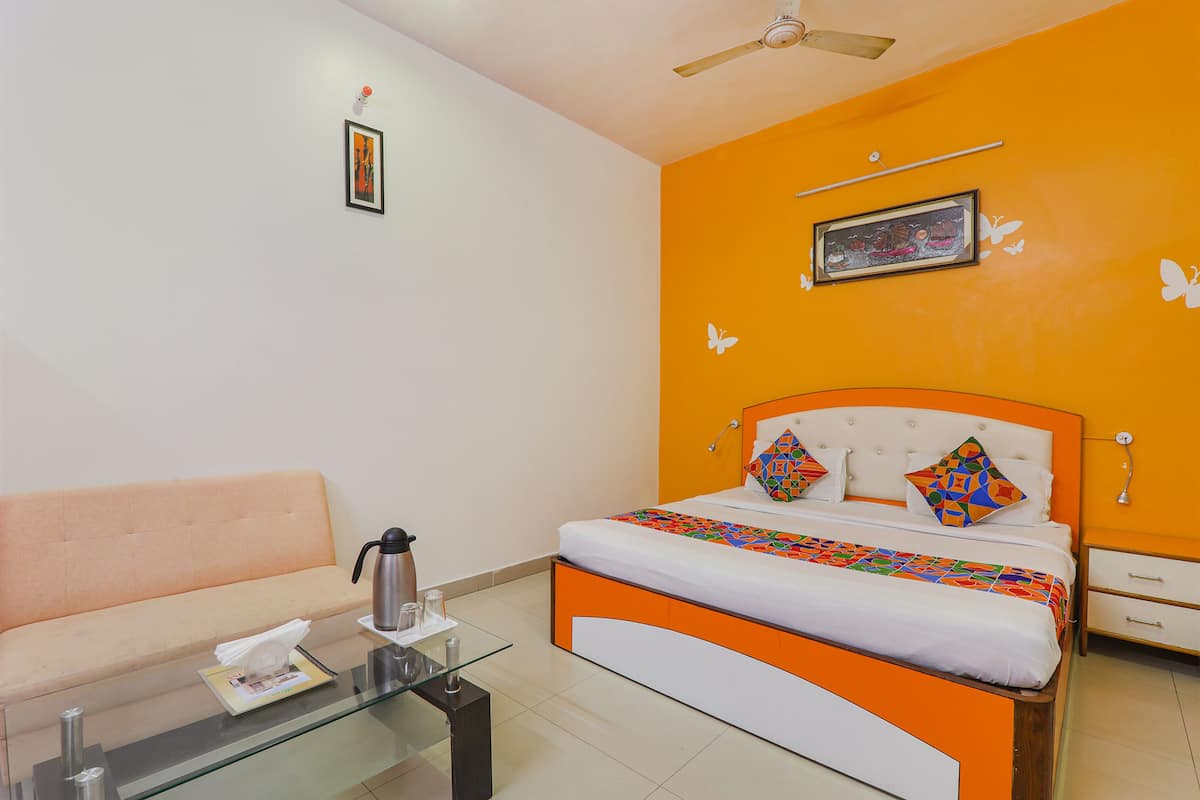Habitación de hotel con cama, sofá, mesa de vidrio y cafetera, y ventilador de techo.