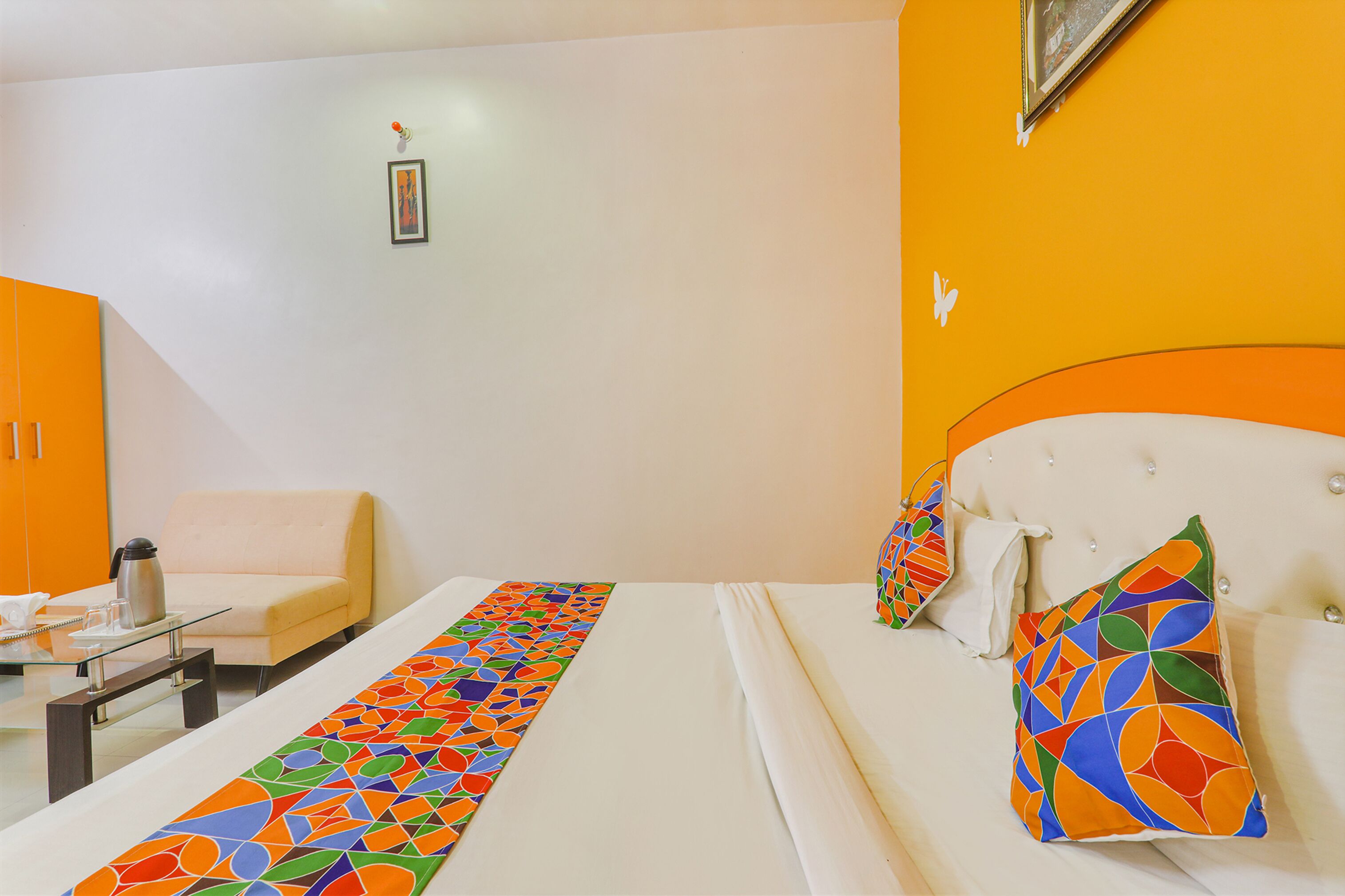 Une chambre d’hôtel avec un lit, un canapé, une table avec une bouilloire et un chemin de table coloré.