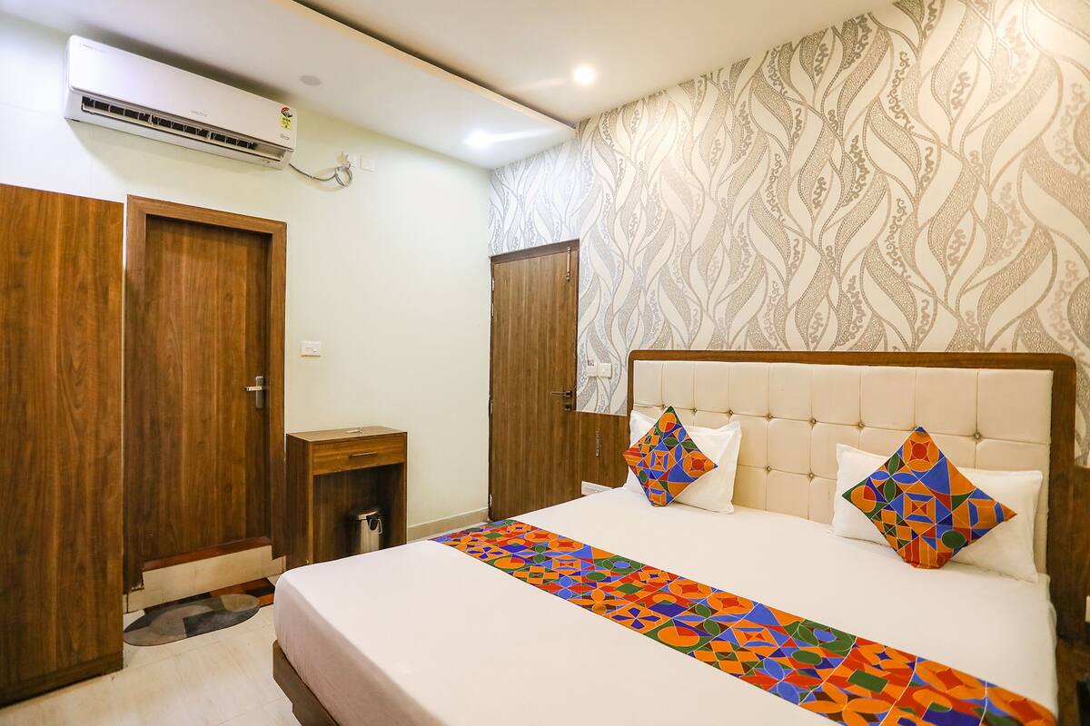 Una habitación de hotel con una cama, dos puertas de madera, una mesita de noche pequeña y un papel tapiz estampado.