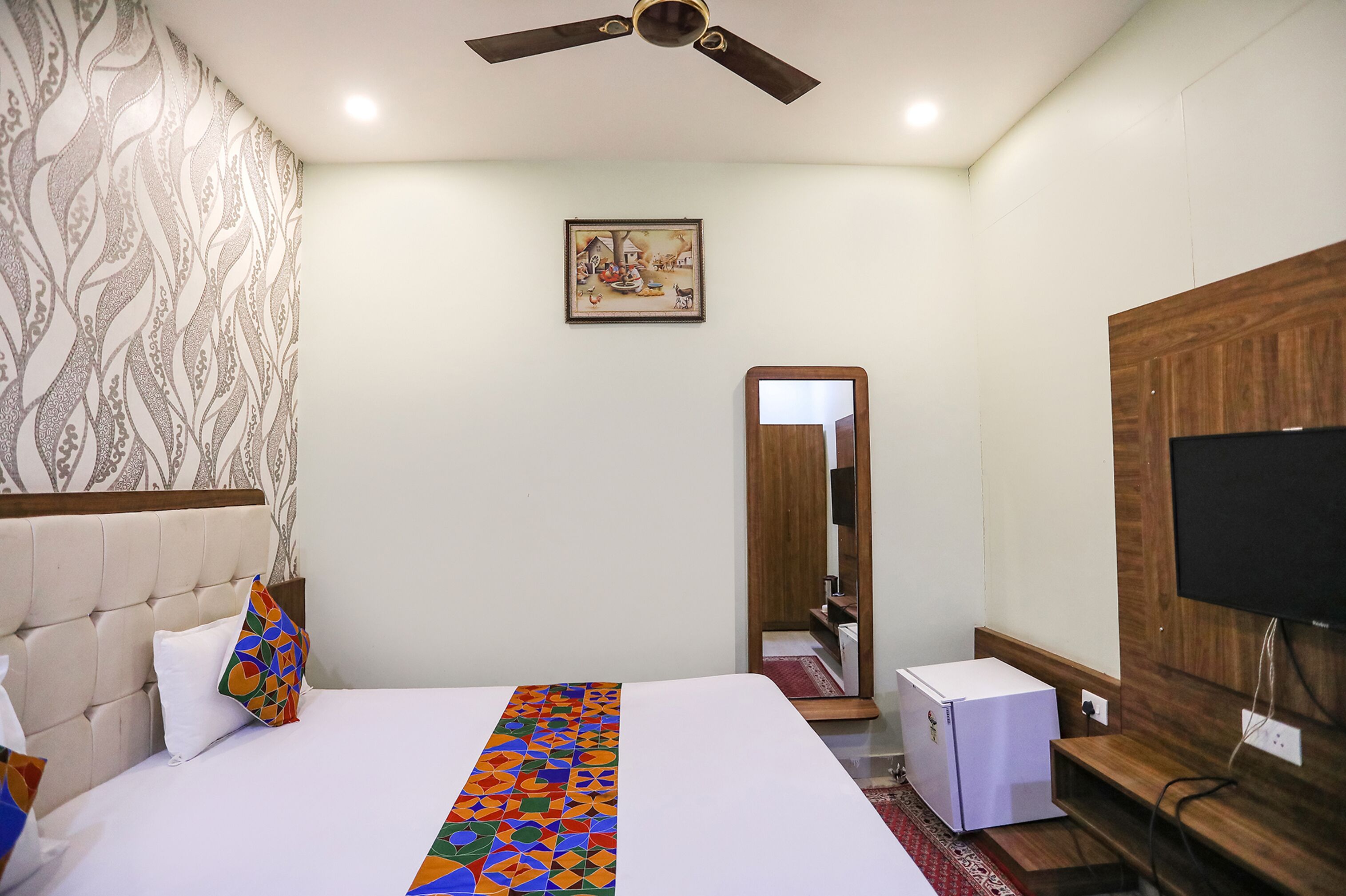 A hotel room with a bed, a ceiling fan, a television, and a small refrigerator.