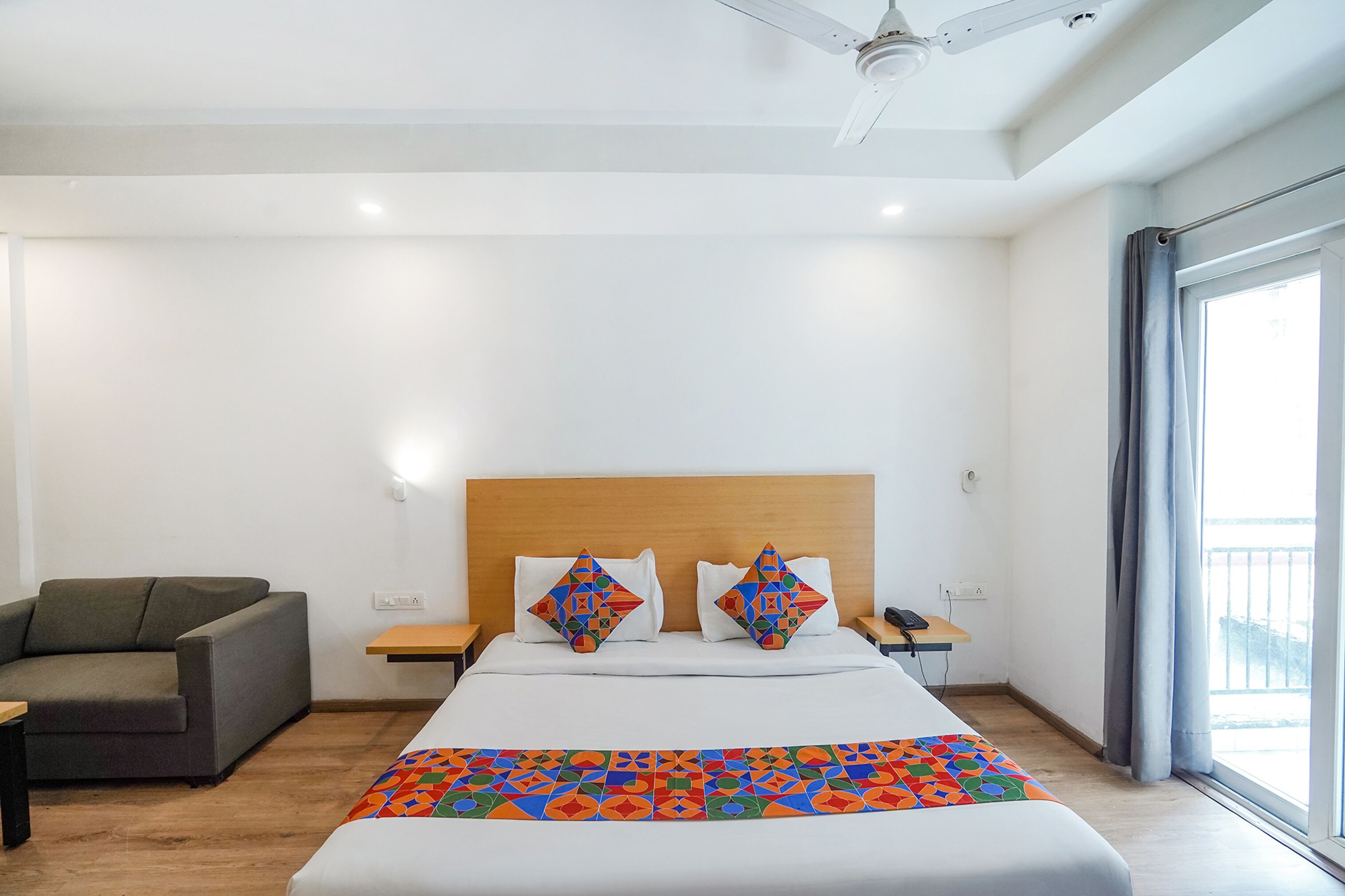 Una habitación de hotel con una cama, un sofá, una mesita de noche y un ventanal con cortinas.