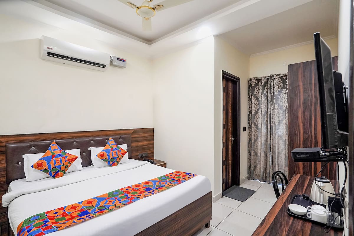 A hotel room with a bed, a television, a desk with a coffee maker, and an air conditioning unit.