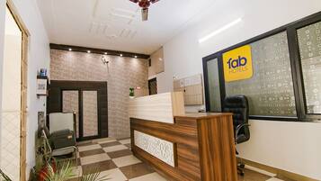 A hotel reception area with a check-in counter, a reception desk, a seating area, and a ceiling fan.