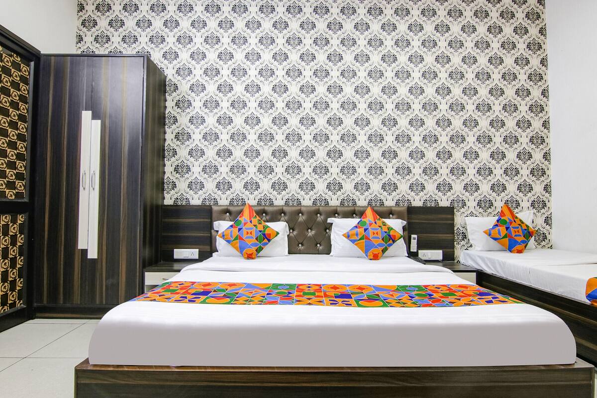 A hotel room with a large bed, two bedside tables, a wardrobe, and patterned wallpaper.
