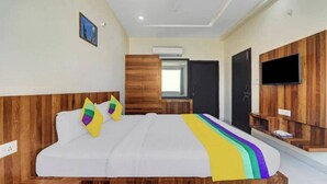 A hotel room with a large bed, wooden headboard, and a TV mounted on the wall. - Hotel Ravi Residency (Bharatpur)