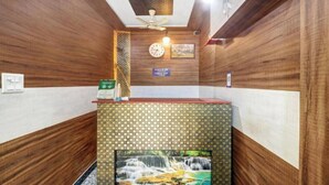 A reception area with a wooden wall design, a clock, a sign indicating check-in and check-out, and a small waterfall painting. - Hotel Ravi Residency (Bharatpur)