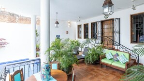 A spacious indoor area with a wooden floor, a green sofa, a dining table, and various potted plants.