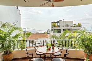 Uma varanda com mesa posta para dois, cercada por plantas em vasos, com vista para a paisagem urbana.